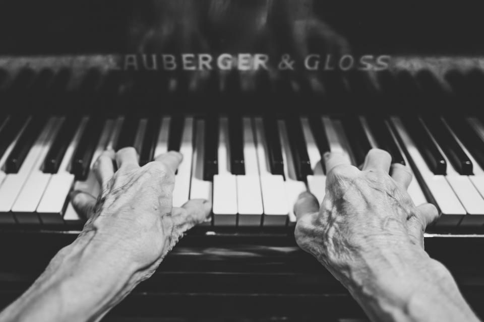 Mature hands resting on the keys of a piano, in black and white