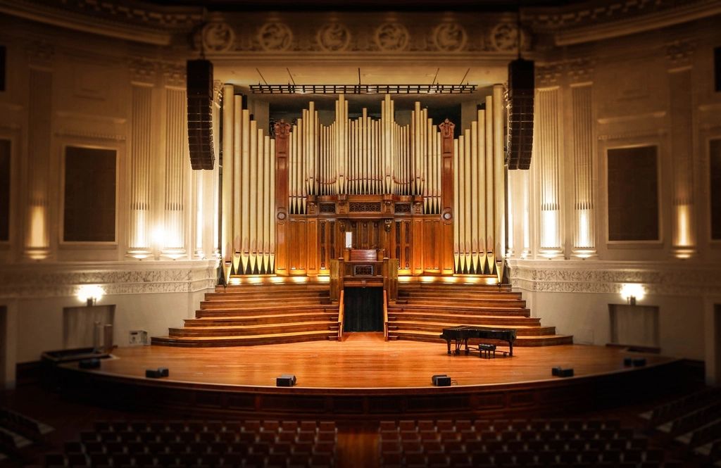 A classical concert hall with a pipe organ above the stage and a grand piano below